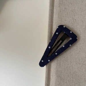 Détail d'une pince à cheveux triangulaire en tissu bleu marine à pois blancs sur lin
