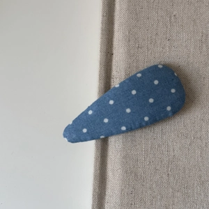 Détail d'une pince à cheveux bleue à pois blancs sur un fond en tissu texturé