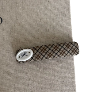 Minimalist brown plaid fabric hair clip with a vintage bow oval accent on a beige base