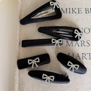 6-piece black satin bow hair clip set with rhinestone accents on beige linen background