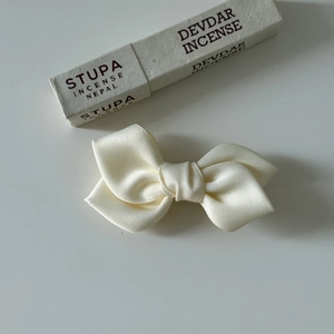Close-up of cream satin bow hair clip showing smooth silk texture and elegant fold design