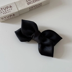 Detailed view of a black satin bow hair clip on a neutral background with soft shadows