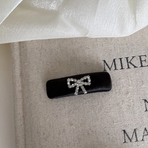 Detail of a black satin rectangular hair clip featuring a delicate silver rhinestone bow