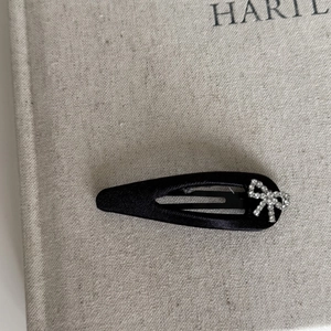 Detail of a black satin ribbon hair clip featuring a delicate rhinestone bow ornament