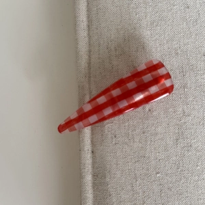 Macro view of a red and white gingham pattern hair clip on a textured linen background