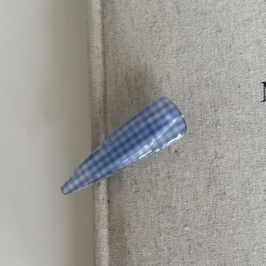 Detailed close-up of blue and white gingham pattern hair clip on neutral linen fabric