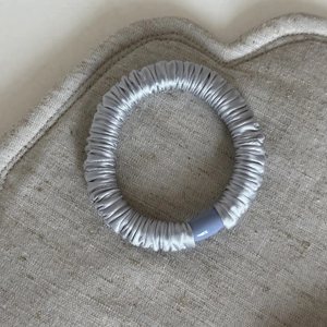 Elastico per capelli in seta grigio argento con clip viola su sfondo di lino