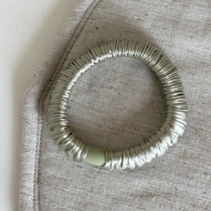 Elastico per capelli in seta verde salvia con lucentezza su sfondo di lino beige