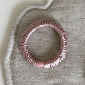 Dettaglio di elastico rosa in raso con trama elastica su un tappetino di lino beige