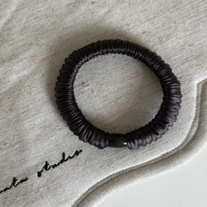 Dettaglio dell'elastico per capelli in seta marrone con decorazione a perla cilindrica nera