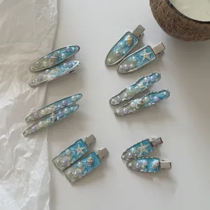Dettaglio di fermagli marini con stella marina blu, conchiglie e perle su bianco