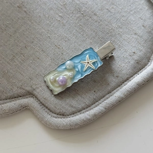 Dettaglio molletta in resina blu oceano con stella marina e perle su base grigia