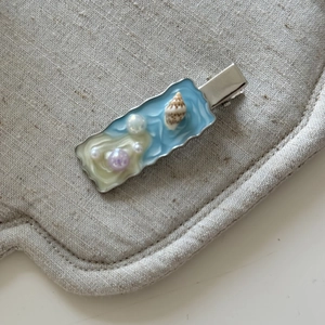 Dettaglio di un fermaglio per capelli stile spiaggia con conchiglie, perle e resina blu