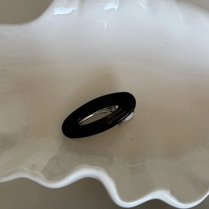 Close-up of black oval acetate hair clip with gold lettering on a shell tray