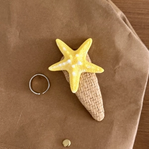 Detail view of a yellow starfish hair clip and a minimalist silver open ring on kraft paper