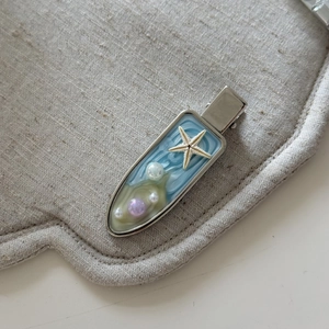 Dettaglio fermaglio per capelli stella marina blu con perle e design marino su tessuto