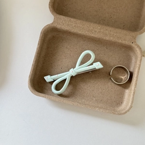 Close-up of a mint green bow hair clip with pink dots in a brown eco-friendly gift box
