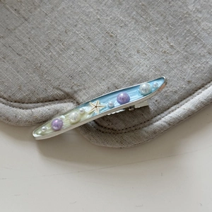 Dettaglio di un fermaglio per capelli a stella marina con resina blu e perle