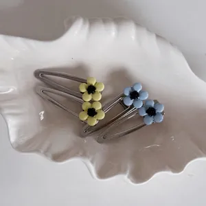 Set of four blue and yellow floral hair clips on a white ceramic shell plate