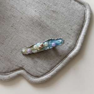 Dettaglio del fermaglio in resina marmorizzata con perle e conchiglia naturale