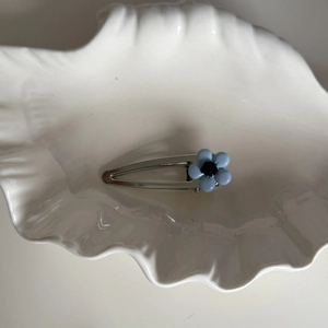Detailed close-up of a blue flower hair clip with silver metal base on a white shell tray