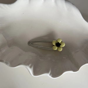 Elegant silver metal flower hair clip with yellow floral accent on white ceramic dish