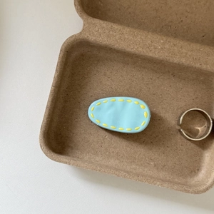 Detail shot of light blue shoe charm accessory in eco-friendly tray with silver ring