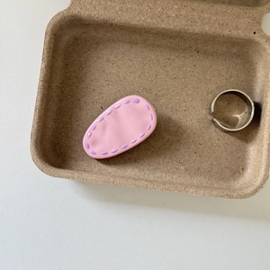Detail of a pink cream-colored hair clip with purple lines and a simple silver ring