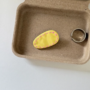 Close-up of a bright yellow oval hair clip with pink dotted patterns on a tray