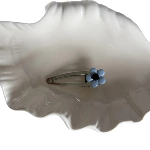 Blue five-petal flower hair clip with silver metal base on a white shell tray
