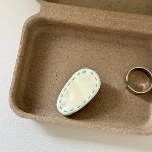 Detail view of cream-colored teardrop hair clip and adjustable silver ring in wood tray