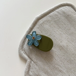 Macro shot of blue flower hair clip with rhinestone and olive green resin base