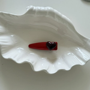 Dettaglio di un fermaglio rosso con cuore in resina viola su vassoio a conchiglia