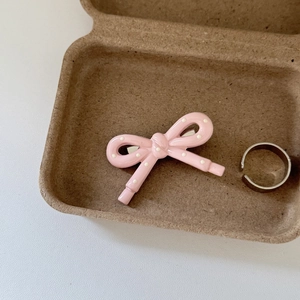Detail of a pink polka dot bow hair clip and minimalist silver ring on white leather