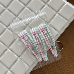 Detailed view of three pink and green plaid BB hair clips on a white ceramic display