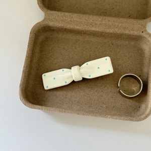 Detail of cream bow hair clip with blue dots and a silver ring in a pulp box