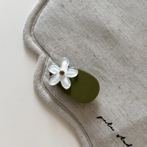 Close-up of olive green hair clip with matte white flower and sparkling rhinestone center