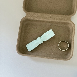 Detail of mint green polka dot bow hair clip and silver open ring in a natural pulp box