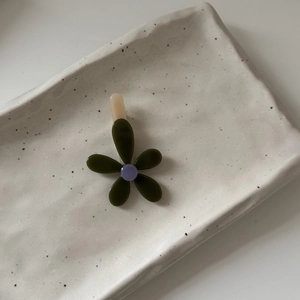 Fermaglio per capelli a fiore con petali verde scuro e centro viola su piatto ceramico