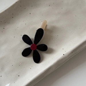 Dettaglio di un fermaglio per capelli a fiore nero lucido con centro rosso su piatto