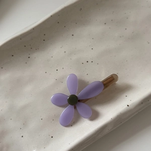 Dettaglio di un fermaglio per capelli a fiore viola con centro verde su vassoio