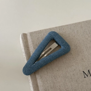 Retro denim blue triangular hair clip with silver metal BB pin on textured book surface