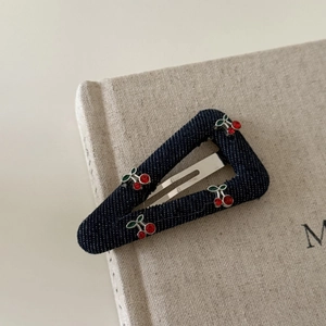 Detailed view of denim triangle hair clip with sparkling cherry rhinestone decorations