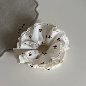 Gros plan d'un chouchou blanc avec motifs cerises et bordure en dentelle ajourée