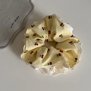 Détail d'un chouchou à carreaux jaunes avec motifs cerises rouges et bordure en dentelle