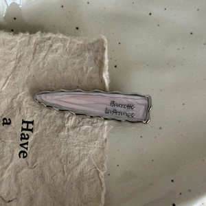 Close-up of a pink marble texture hair clip with silver wavy edges and letter print