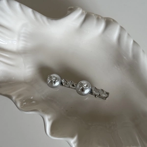 Barrette argentée avec nœud et cristaux sur un plateau décoratif en forme de coquillage