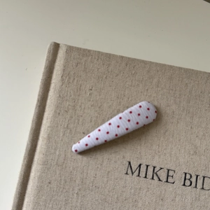 Detailed view of white fabric hair clip with red polka dots on a linen book background