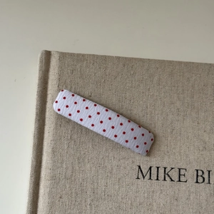 Close-up of a rectangular red polka dot fabric hair clip on a beige textured book