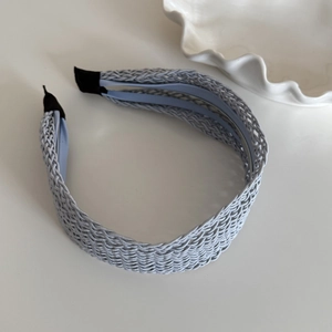 Détail d'un serre-tête tressé bleu clair montrant la texture croisée et les embouts noirs